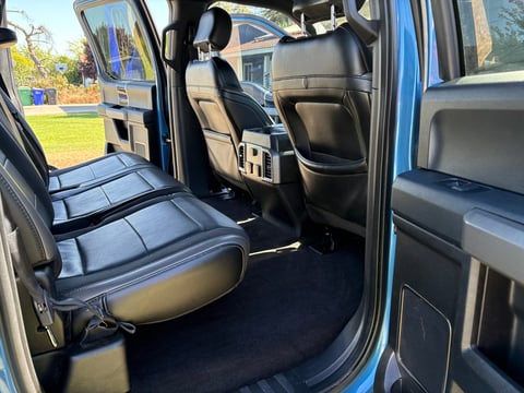 Interior of blue pickup truck showing open driver side door with black and gray leather seats and dark floor mat