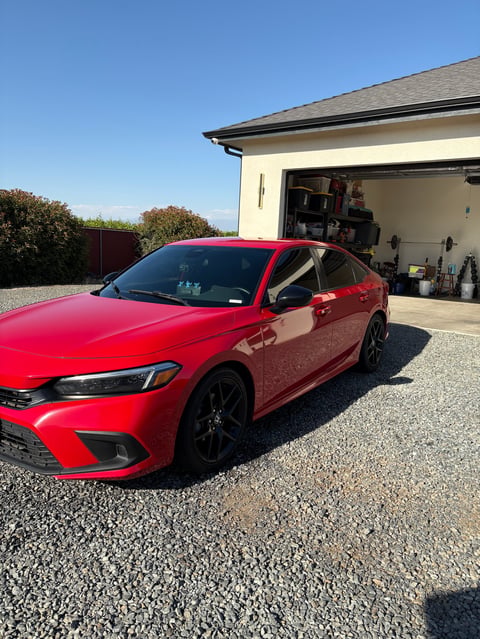 Red sedan parked in driveway in front of open garage on clear sunny day