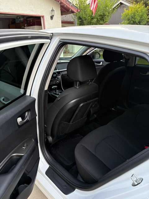 Interior view of white car with open passenger door showing black leather seats and dashboard, garage in background