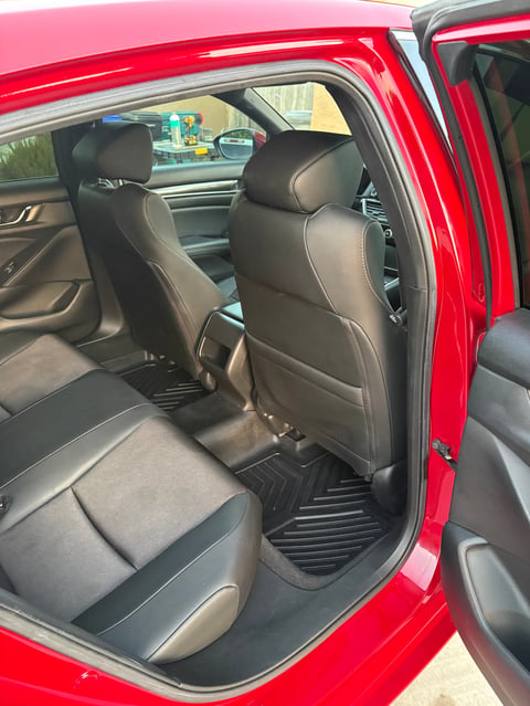 Interior of a red car with open door showing black leather seats and dashboard with other vehicles visible outside