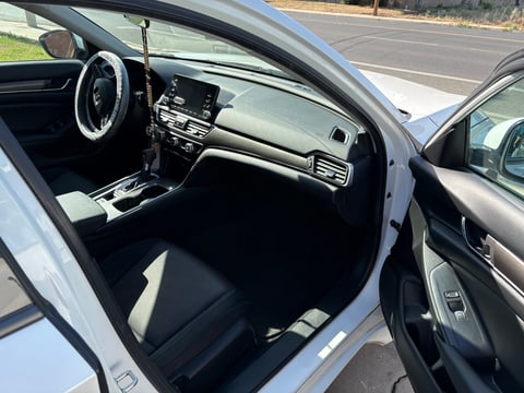 Interior view of white sedan with door open showing dashboard, steering wheel, and center console on a road