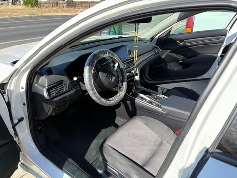 Interior view of a white vintage car showing steering wheel, dashboard, and gray seat with door open