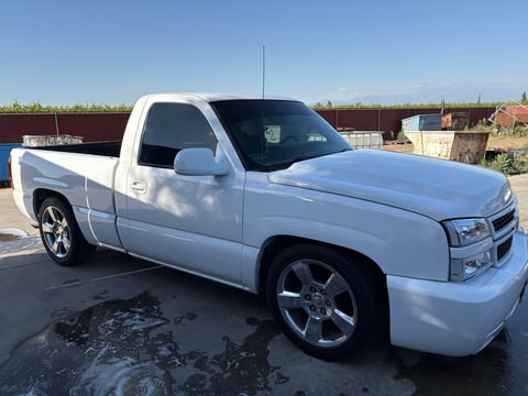White customized pickup truck with chrome wheels parked on asphalt in an outdoor lot