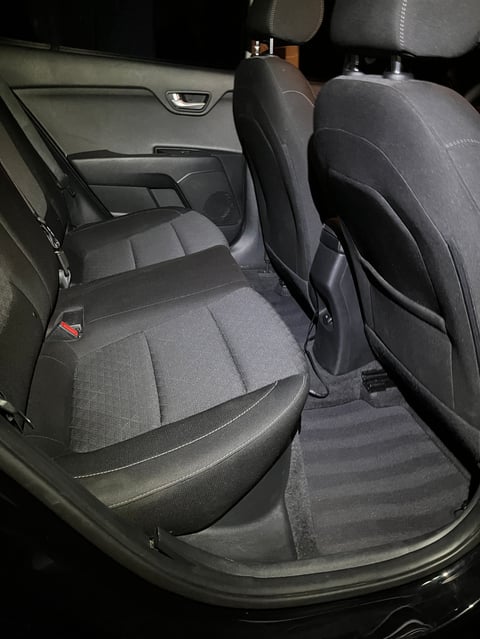 Interior view of a cars rear passenger seats with gray and black upholstery, door panel visible, and floor mat