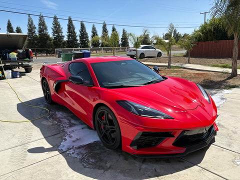 Bright red sports car parked on concrete lot with trees and fencing in background on sunny day