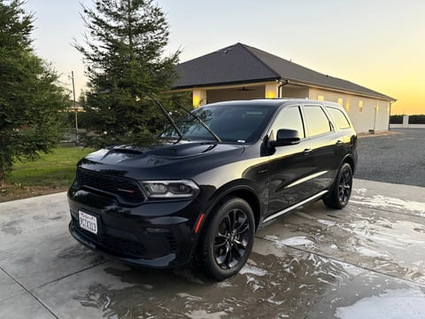 Black Dodge Durango SUV parked in driveway with open hood, modern house in background at sunset