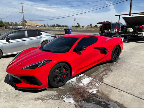 Bright red sports car parked at an outdoor venue with other vehicles visible in background