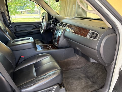 Interior of classic truck with black leather seats, wood-grain dashboard trim, and steering wheel visible through windshield with outdoor background
