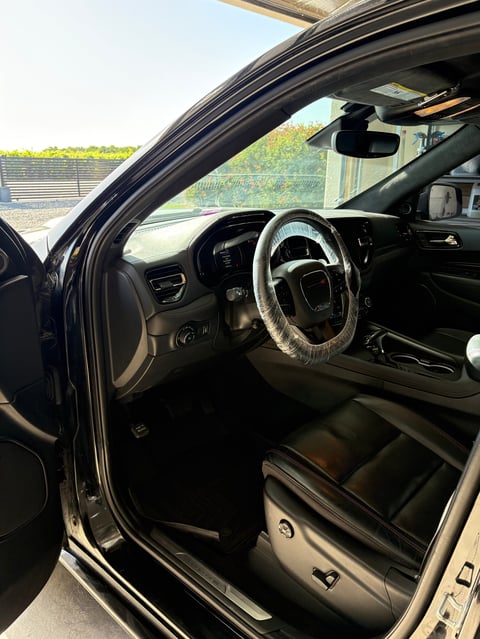 Interior view of a car showing the steering wheel, dashboard, and open drivers side door with a sunny outdoor landscape visible