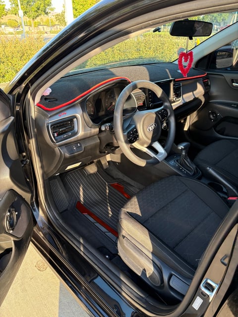 Interior of a car with tan steering wheel, black and red seats, dashboard, and a red air freshener hanging from the rearview mirror