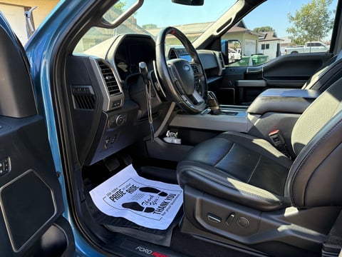 Interior of a blue truck with black and tan leather seats, steering wheel, dashboard, and an open driver door showing the cabin