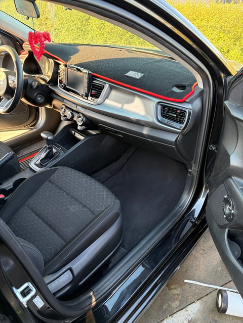 Interior view of a car with red trim accents on dashboard, steering wheel, and bow on rearview mirror