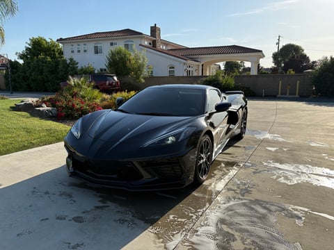 Black sports car parked in driveway of large white house on sunny day
