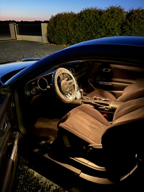 Interior of blue convertible car with tan leather seats and steering wheel cover at dusk