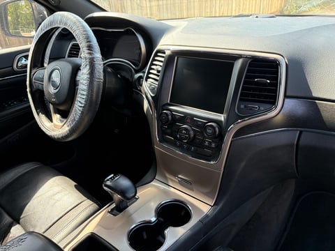 Interior of SUV showing steering wheel, touchscreen dashboard, cup holders, and black leather seats