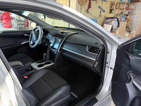 Interior of white car with open driver door showing steering wheel, dashboard, black seats, and garage in background