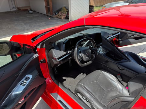 Red convertible sports car with drivers door open, showing gray interior and steering wheel in a garage