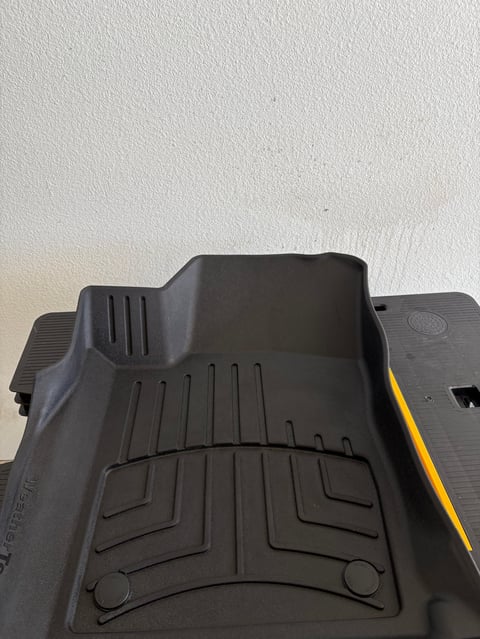 Black rubber car floor mat with channel design and yellow stripe on white background