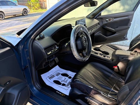 Interior of blue car with open door showing black leather seats, steering wheel with cover, and manual on drivers seat