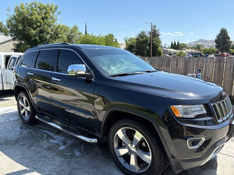 Black Jeep Grand Cherokee SUV parked on driveway with residential neighborhood in background
