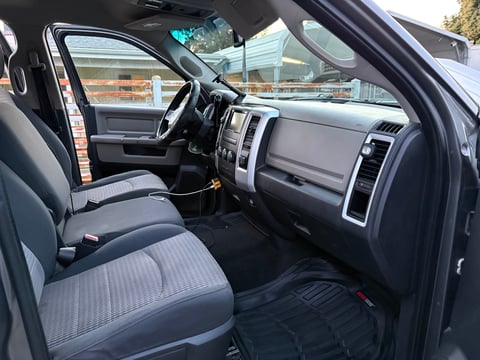 Interior view of a truck cabin with gray and black cloth seats, steering wheel, dashboard with touchscreen display, and automatic transmission gear shift