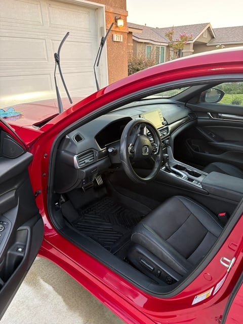 Red car with driver door open showing black leather interior and steering wheel in residential driveway
