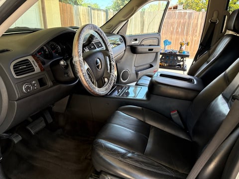Interior view of a truck cab with black leather seats, steering wheel, and dashboard visible through open doors