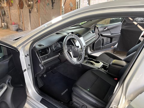Interior of a white car showing steering wheel, dashboard, black seats, and open drivers side door in a garage workshop